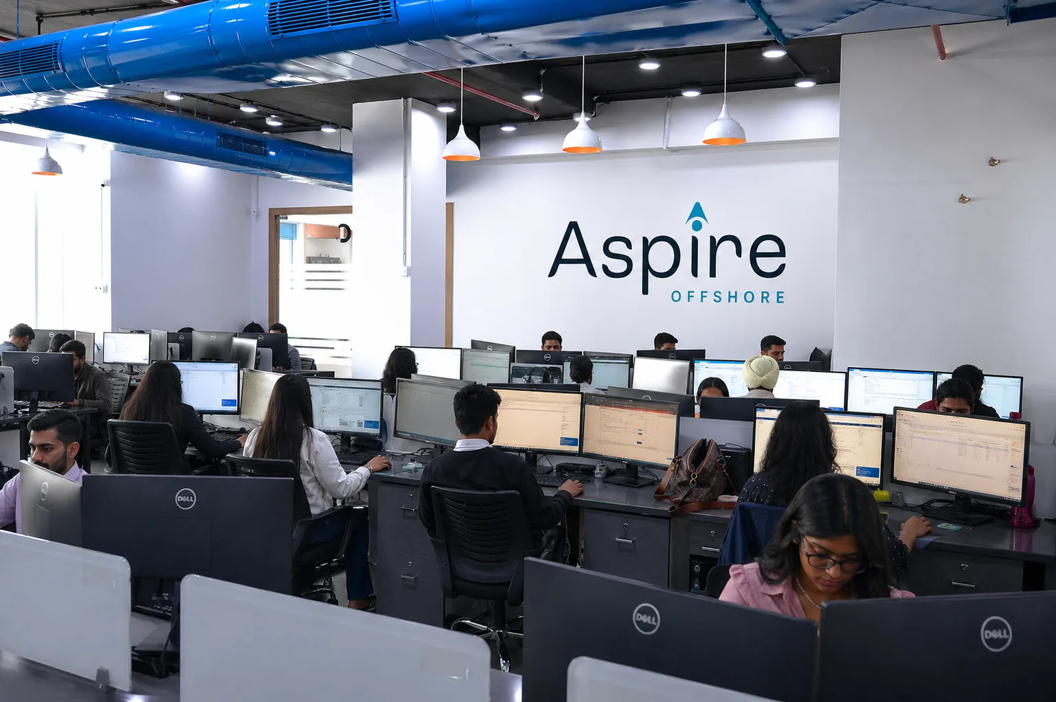 The Aspire Offshore team working at their workstations in our offshore delivery office, beneath the Aspire Offshore wall branding